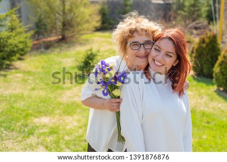 Adult daughter gives flowers to her mother outside, in the courtyard of the house. Spending time together, celebrating at home on weekends. Mothers Day. Warm intergenerational relationships