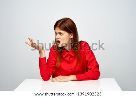 Emotional woman in a red shirt gesticulates with her hands and looks away         