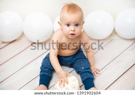 One year baby birthday party. Baby eating birthday cake. The boy on a light background celebrates and smash the cake.