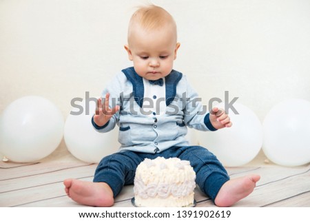One year baby birthday party. Baby eating birthday cake. The boy on a light background with ballons celebrates