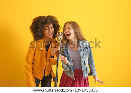Teenage girls with microphone singing against color background Royalty-Free Stock Photo #1391935358