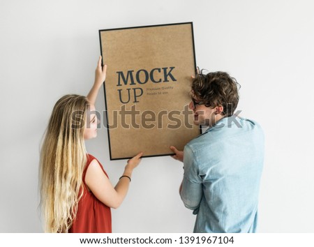 Couple hanging a photo frame mockup on a white wall