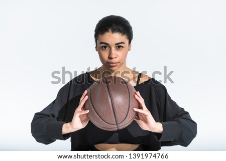 beautiful sportive african american girl with brown ball looking at camera on white