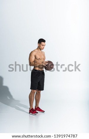 handsome shirtless mixed race man in black shorts and red sneakers holding ball on white