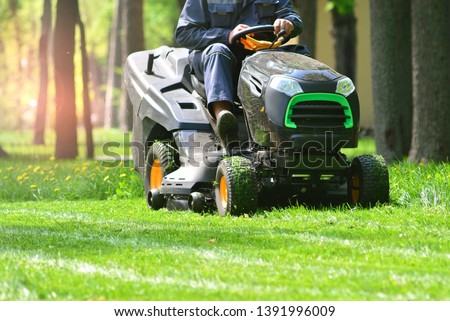 Professional lawn mower with worker cutting the grass in a garden Royalty-Free Stock Photo #1391996009