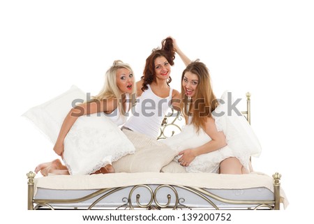 Happy cheerful girls having fun sitting on the bed on a white background. Pyjamas party.