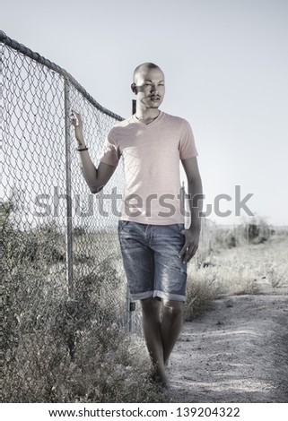 Full length vertical photo of young man wearing casual summer clothing posing beside metal fence.  Fashion style portrait.  Cross processed, reduced saturation.