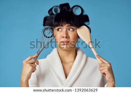 portrait of housewife with hair curlers holding a head and a whisk and a wooden spoon on a blue background                              