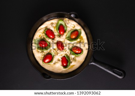 Food concept rising dough for Homemade organic Focaccia in skillet iron pan on black background with copy space