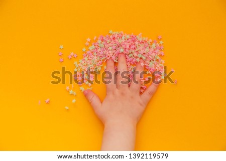 small colorful stars on a yellow background. children's hand touches multicolored stars