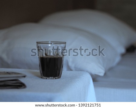 Hot coffee in a clear glass is placed on a table in the white bedroom with morning newspaper.