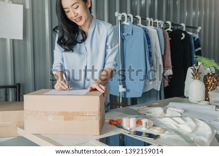 Young business woman working online e-commerce shopping at her shop. Young woman seller prepare parcel box of product for deliver to customer. Online selling, e-commerce.