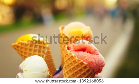Someone keeps fruit ice cream in wafer cones, close-up. against a blurred pedestrian street in spring or summer