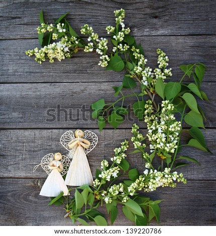 Composition from the bouquet of white lilac and two straw angels on wooden  background