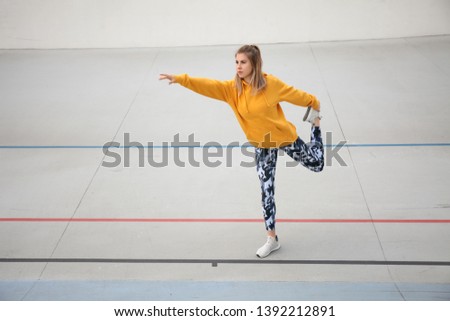Pretty woman in yellow top and military leggings does warm-up before outdoor sports.