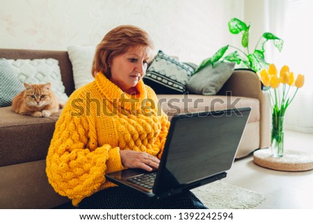 Senior woman using laptop at home relaxing with cat. Elderly people learning modern technology