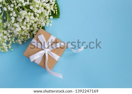 Gift box with white ribbon  and lilies of the valley on the blue background.Top view.Copy space for text.