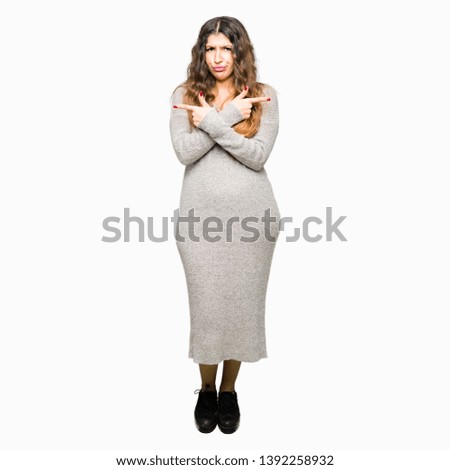 Young beautiful woman wearing winter dress Pointing to both sides with fingers, different direction disagree