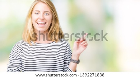 Beautiful young woman wearing stripes sweater over isolated background with a big smile on face, pointing with hand and finger to the side looking at the camera.