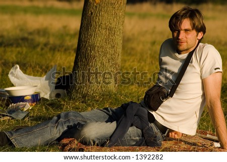 young man with mini camera bag sitting on grass