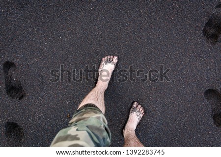 Men's feet are on the volcanic black sand.