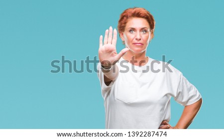 Atrractive senior caucasian redhead woman over isolated background doing stop sing with palm of the hand. Warning expression with negative and serious gesture on the face.