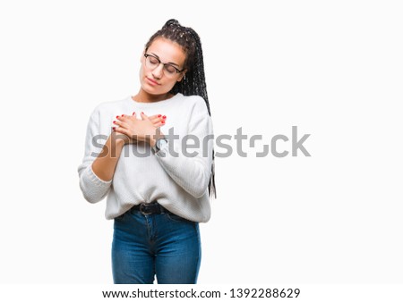 Young braided hair african american girl wearing glasses and sweater over isolated background smiling with hands on chest with closed eyes and grateful gesture on face. Health concept.