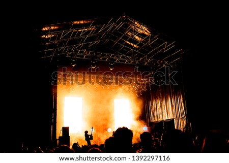 Picture of a lot of people enjoying night perfomance, large unrecognizable crowd dancing with raised up hands and mobile phones on concert. nightlife. Silhouette of musician or singer