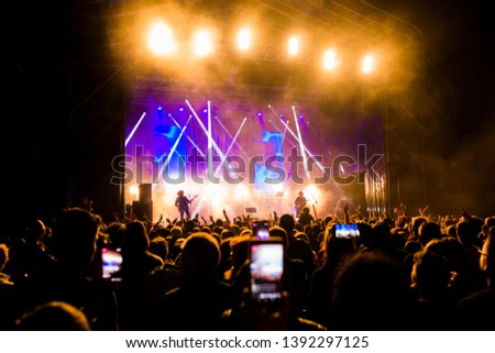Picture of a lot of people enjoying night perfomance, large unrecognizable crowd dancing with raised up hands and mobile phones on concert. nightlife