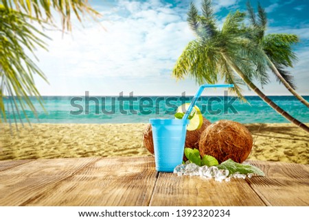 Cold drink on wooden table. Summer landscape of beach with palms and ocean. Sunny warm day and free space for your decoration. 