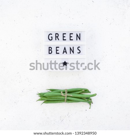 Creative scandinavian style flat lay top view of fresh green beans and text in lightbox on white concrete table background copy space. Minimal house cooking concept template for blog or recipe book