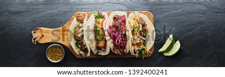four mexican street tacos with fish barbacoa and carnitas shot in panoramic composition on top of serving wooden board