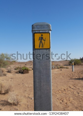 A metal pole with a hiking marker in the desert near Mound Springs on the Oodnadatta Track with desert plants, sand & other poles marking the trail on soft focus on the background South Australia