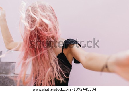 Wonderful long-haired woman in black dress fooling around during studio photoshoot. Indoor portrait of emotional girl with pink hair expressing happiness and dancing.