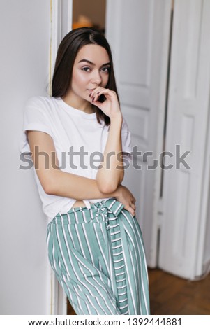 Slim interested girl in white t-shirt posing in her apartment. Indoor photo of fascinating woman relaxing at home.