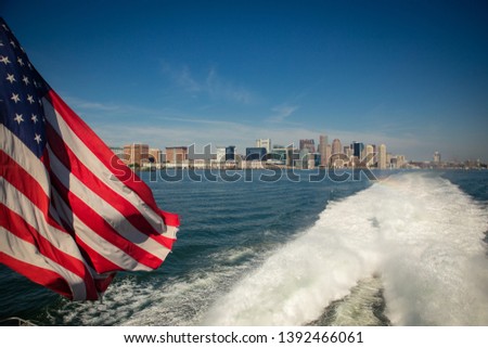 American flag in the breeze as seen from a fast ferry with the Boston skyline in the background.