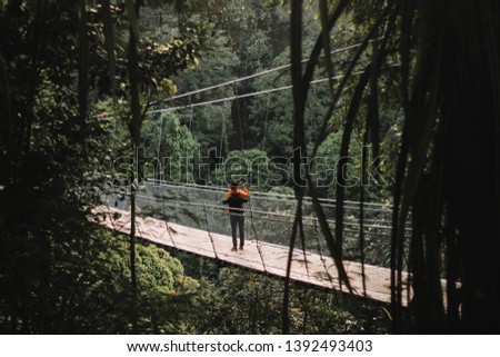 A man is being framed with trees while taking picture of the scenery around Situgunung Suspension Bridge, the longest Suspension Bridge located in the middle of the forest of Indonesia.