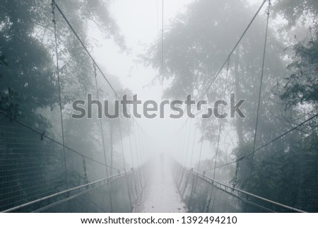 A man is hardly seen standing on Situgunung Suspension Bridge, the longest Suspension Bridge located in the middle of the forest of Indonesia, during a foggy situation after the rain.