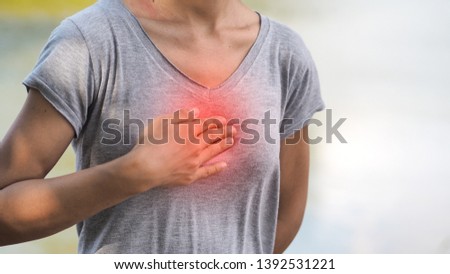 The woman wearing a gray shirt in the garden is using her hands to hold the chest, showing symptoms of burning in the chest caused by acid reflux.