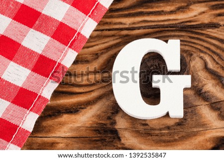 Letter G of the alphabet - Red checkered cloth tablecloth on rustic wood background