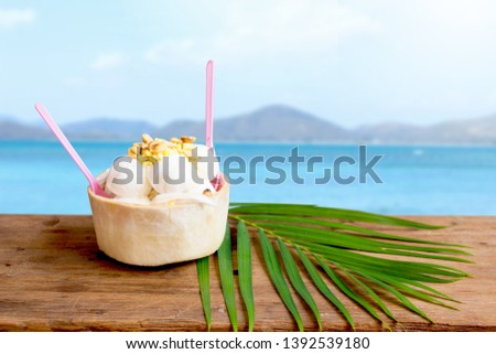 Coconut Milk Ice Cream in the coconut shell on rustic wooden table with blur summer beach and blue sky background.
Thai dessert concept. 