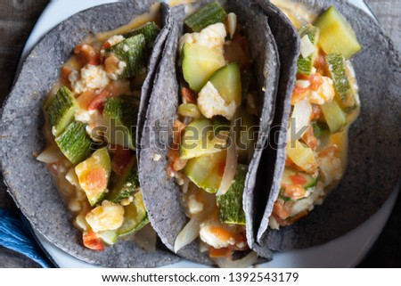 Mexican zucchini stew  and blue tortilla on wood background