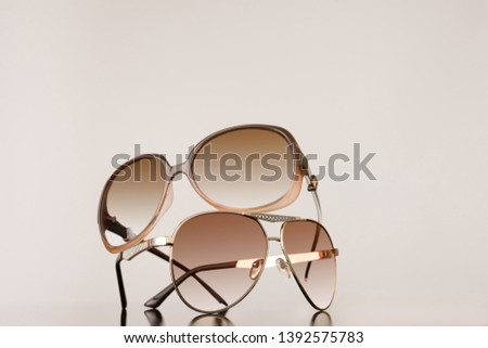 Two pairs of womens sunglasses stacked on top of each other with plain background - summer fashion concept image with copy space for text. Royalty-Free Stock Photo #1392575783