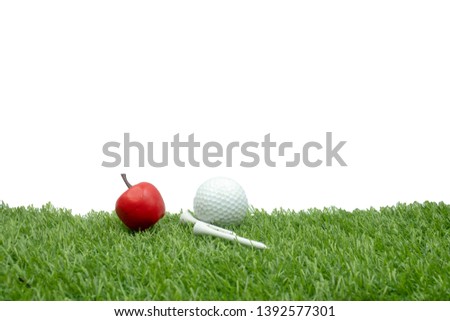 Golf ball with apple and tee on green grass isolated on white background
