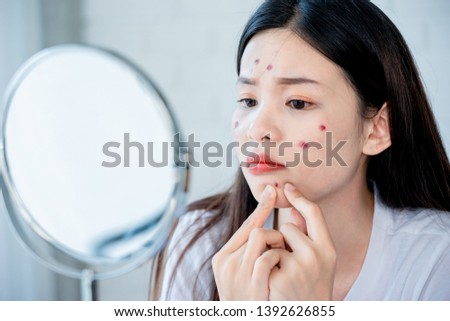 Asian teenage woman  looking at mirror and squeeze acne problem on her face, skin care concept. Royalty-Free Stock Photo #1392626855