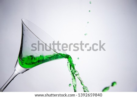 pouring green martini cocktail, liquor into a glass, colour drink splash out of glass.