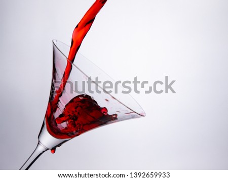 pouring red martini cocktail, red wine, liquor into a glass, colour drink splash out of glass.
