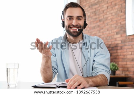 Young man with headset looking at camera and using video chat in home office Royalty-Free Stock Photo #1392667538