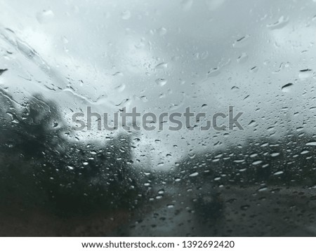 rain drops on car's windscreen with blurred stormy gray sky, hardly to see a car in front, and trees along the road
