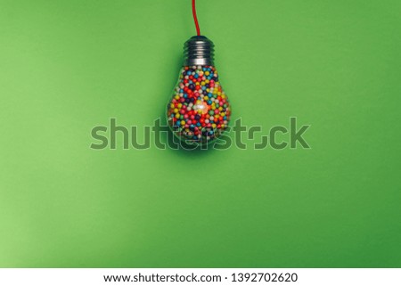 Lightbulb filled with multi colored ball on a green background behind. Best idea concept.